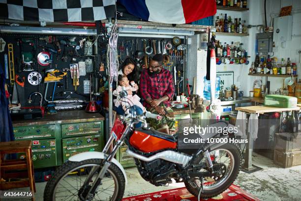 young family in motorcycle workshop. - motorbike flag stock-fotos und bilder