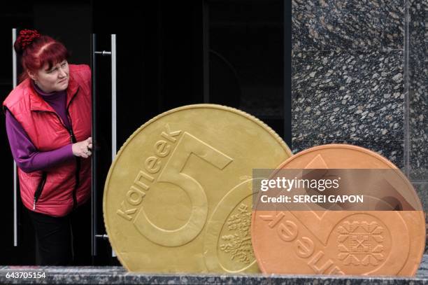 Woman looks out of the door next to a giant Belarusian ruble coin monument near the Ministry of taxes-and-duties in Minsk, on February 22, 2017.