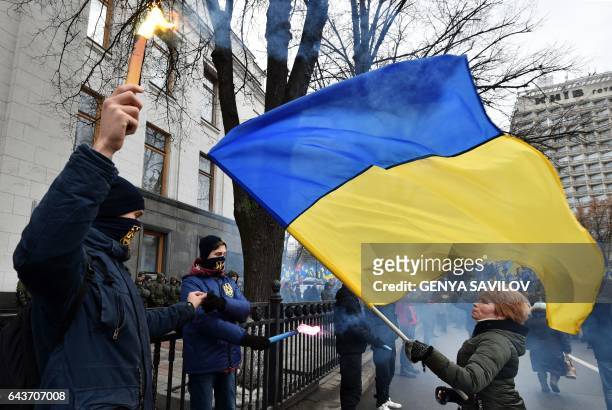 Supporters of various Ukrainian nationalist parties light smoke bombs while a woman waves a Ukrainian national flag in front of them during a rally...
