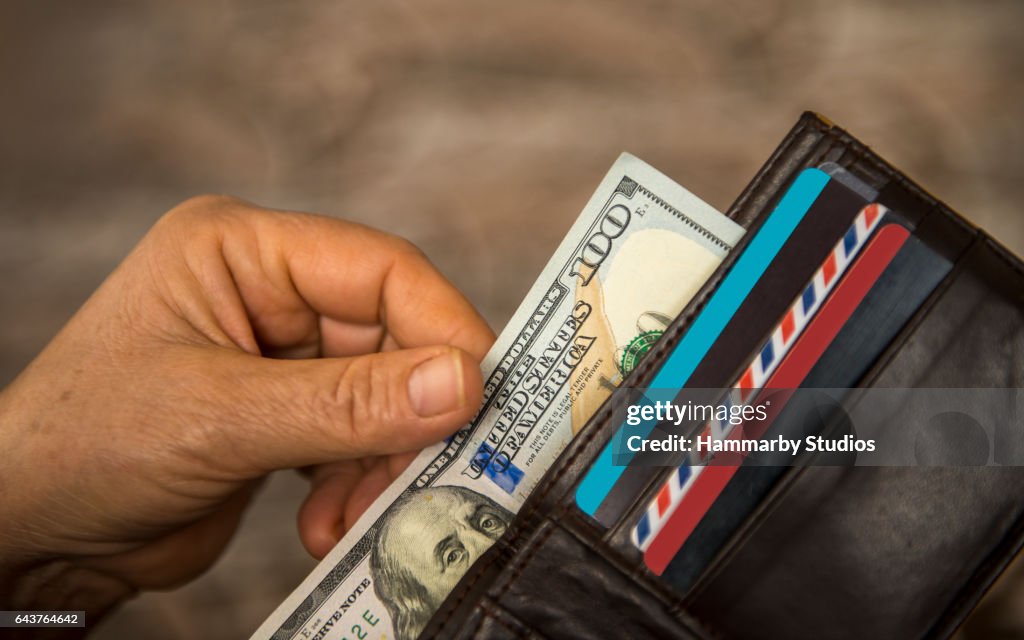 Unrecognizable mature man putting USA Dollar bill into wallet
