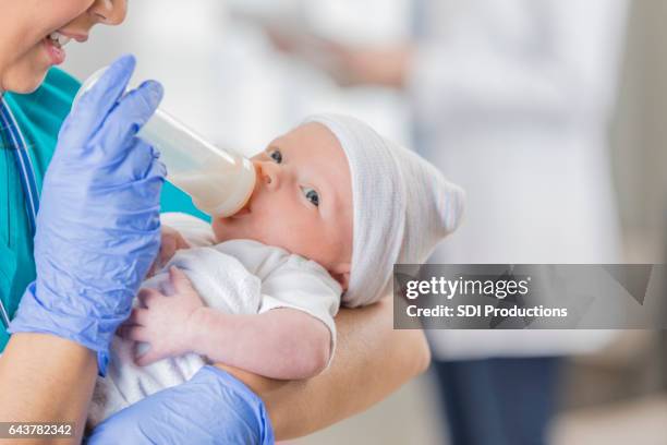 adorable infant takes a bottle in hospital nursery - nurse hat stock pictures, royalty-free photos & images