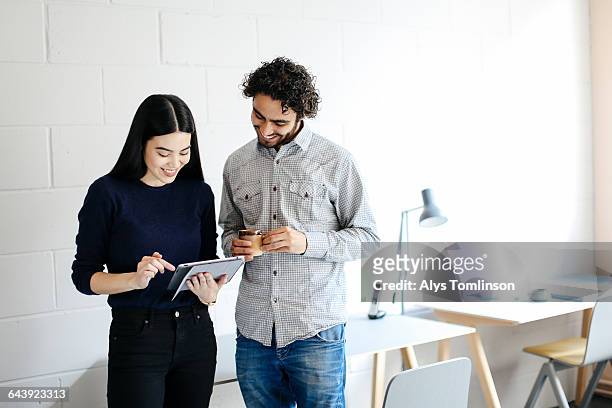 young man and woman smiling and looking at tablet - creative collaboration holding stockfoto's en -beelden