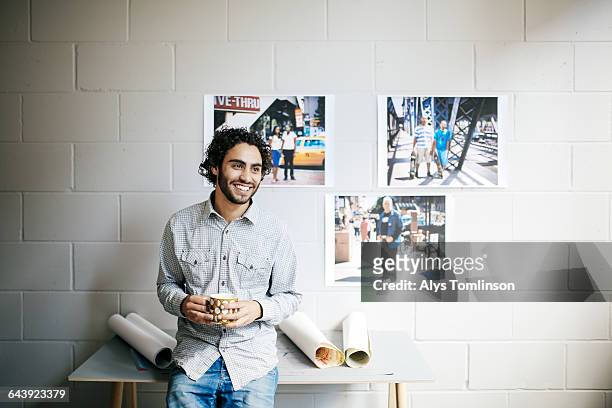 young man smiling and drinking coffee in studio - photo wall stock pictures, royalty-free photos & images