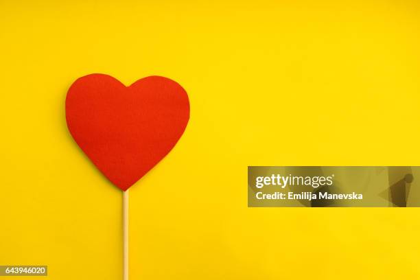 red paper heart on yellow background - heart month stockfoto's en -beelden