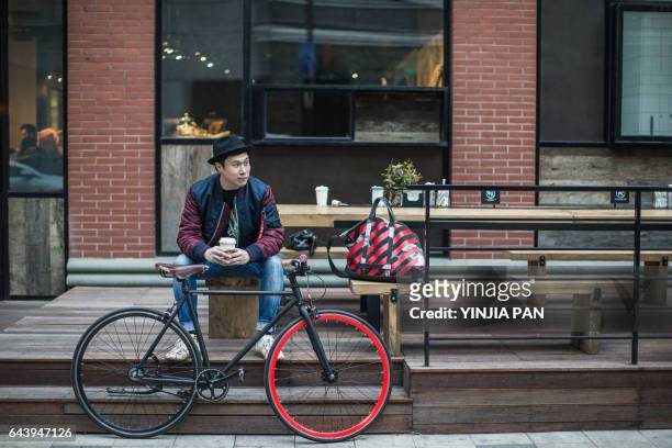 young man sitting on the bench holding cup of coffee - about you fashion week - fotografias e filmes do acervo