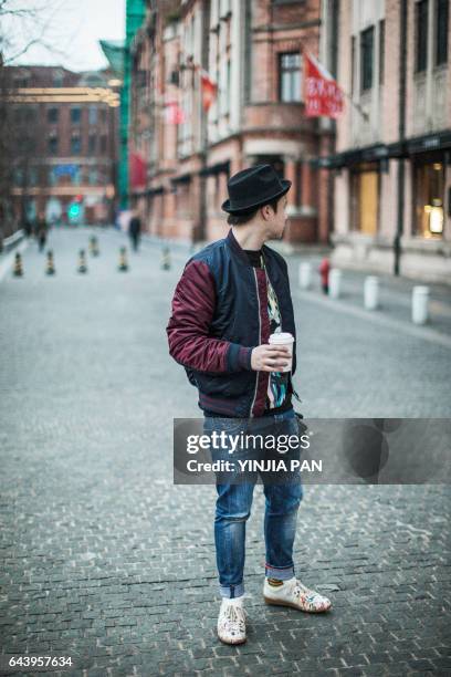 young man walking outdoors, carrying coffee cup and gloves - man looking back stock pictures, royalty-free photos & images