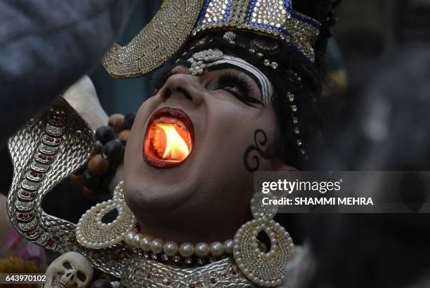 An Indian Hindu man dressed as Lord Shiva holds a lit candle in his mouth as he takes part in a religious procession ahead of the Maha Shivratri...