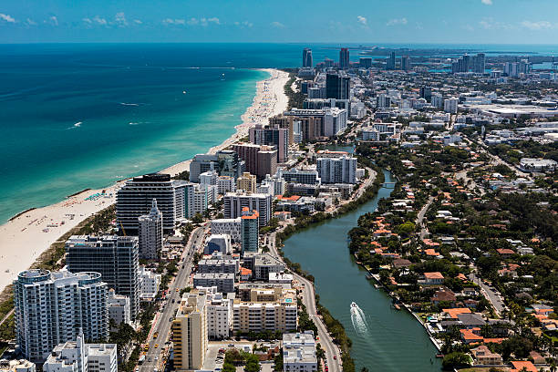 Aerial view of South Beach Miami Florida cityscape with buildings along the beach on a beautiful sunny day, people on beach and ocean, Collins Ave., and boat on Indian Creek
