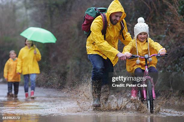 family out in rain and puddles with bike - mother protecting from rain stock-fotos und bilder