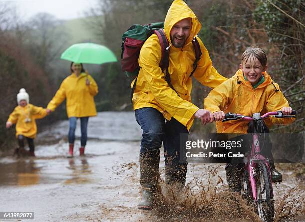 family out in rain and puddles with bike - family in rain stockfoto's en -beelden