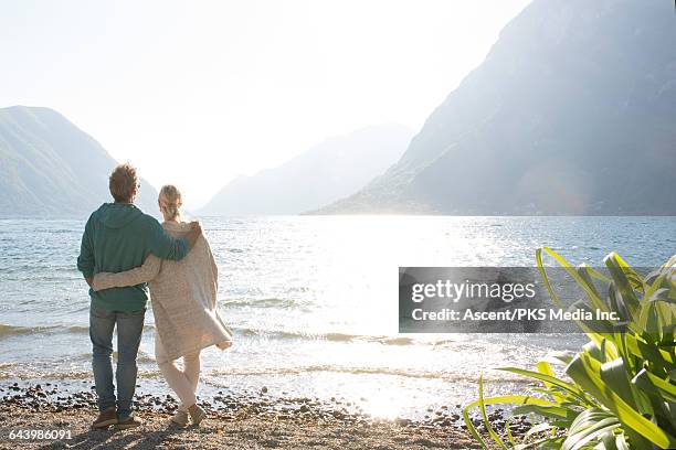 couple pause on beach, look out to lake behind - couple jeans shirt stock-fotos und bilder