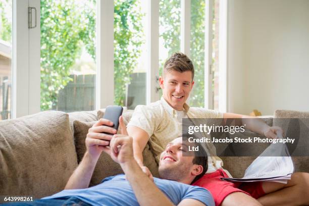 caucasian gay couple using cell phone and reading newspaper - melbourne newspaper stock pictures, royalty-free photos & images