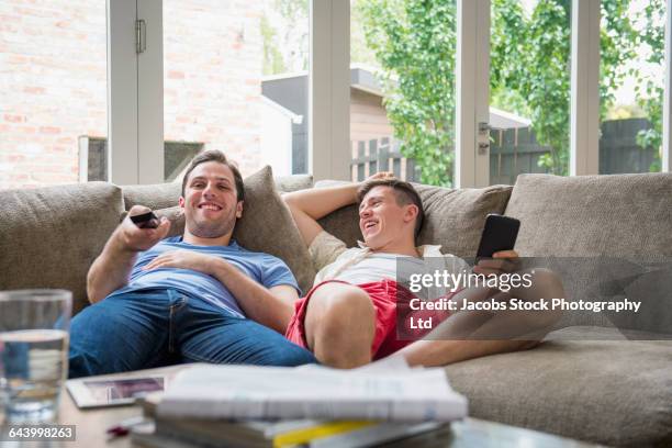 caucasian gay couple watching television on sofa - melbourne homes stockfoto's en -beelden