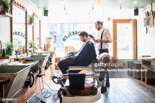 caucasian stylist cutting hair of customer in barber shop - barbero peluquería fotografías e imágenes de stock