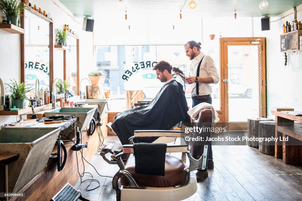 Caucasian stylist cutting hair of customer in barber shop