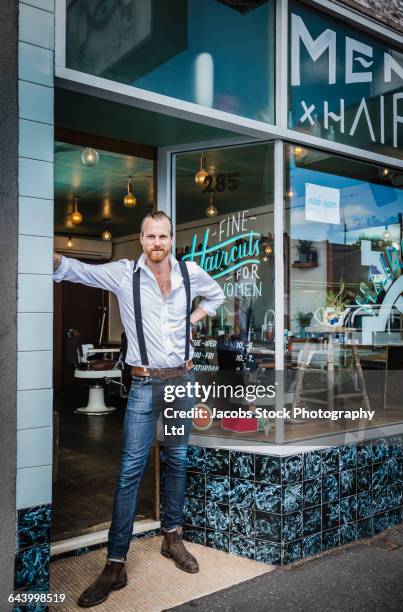 caucasian stylist standing in barber shop doorway - barber shop stock-fotos und bilder