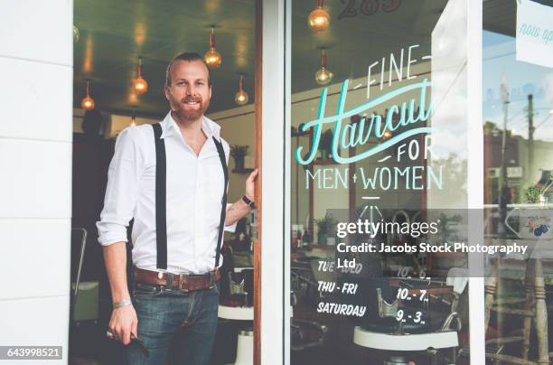 caucasian stylist standing in barber shop doorway - barber shop stockfoto's en -beelden