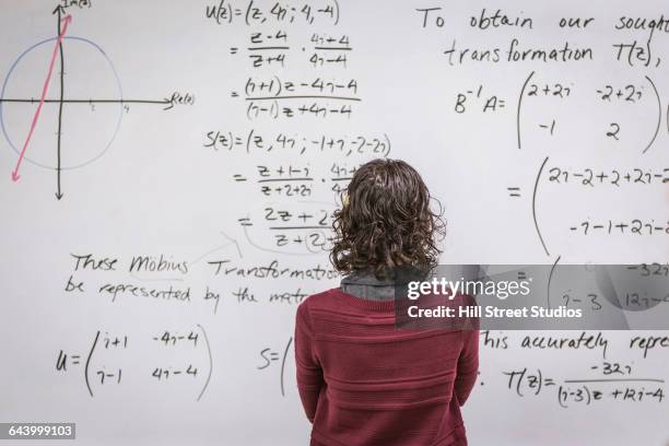 caucasian professor examining equations on whiteboard - wiskunde stockfoto's en -beelden