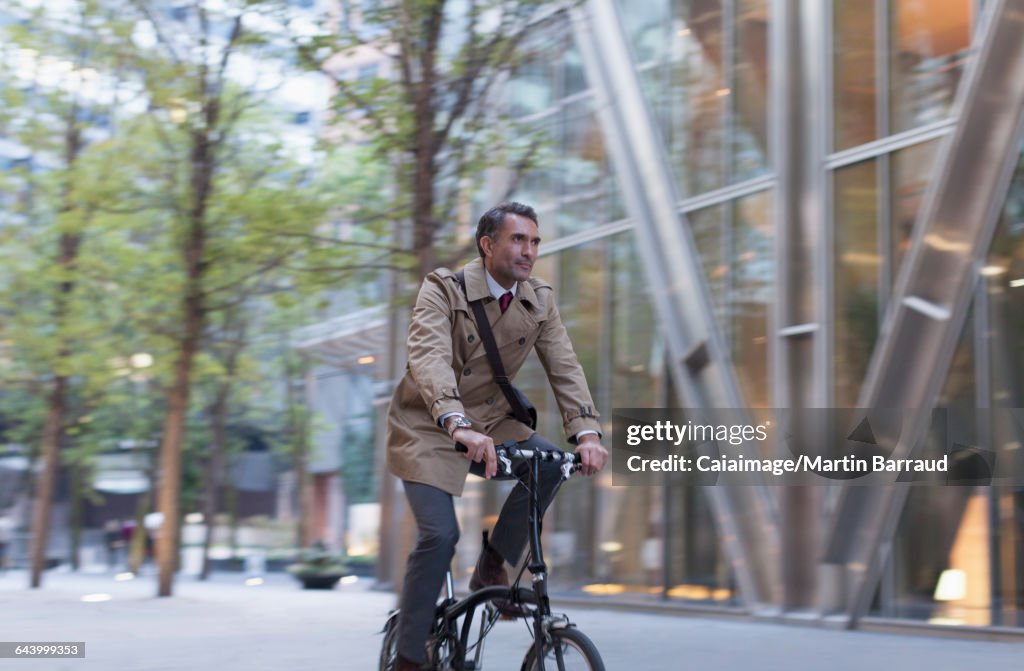 Corporate businessman riding bicycle outside modern building