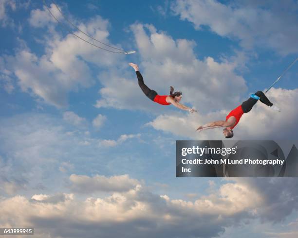 trapeze artists jumping in sky - trapeze stock-fotos und bilder