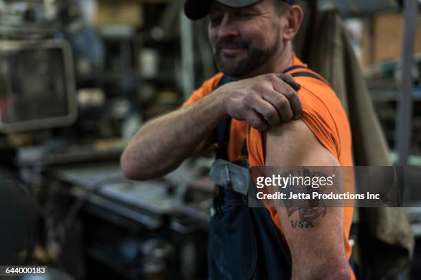 caucasian worker displaying tattoo in factory - mostrare foto e immagini stock