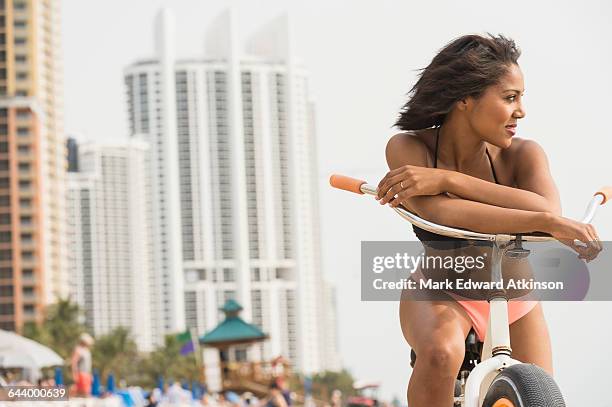 african american woman sitting on bicycle on beach - miami fahrrad stock-fotos und bilder