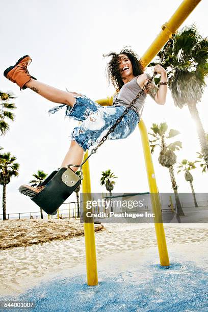 mixed race woman standing on swing at beach - schaukel stock-fotos und bilder