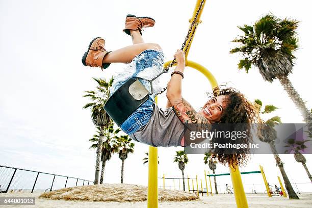 mixed race woman playing on swing at beach - woman on swing stock pictures, royalty-free photos & images