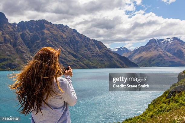 caucasian woman photographing mountains and lake, queenstown, otago, new zealand - lake auburn stock pictures, royalty-free photos & images