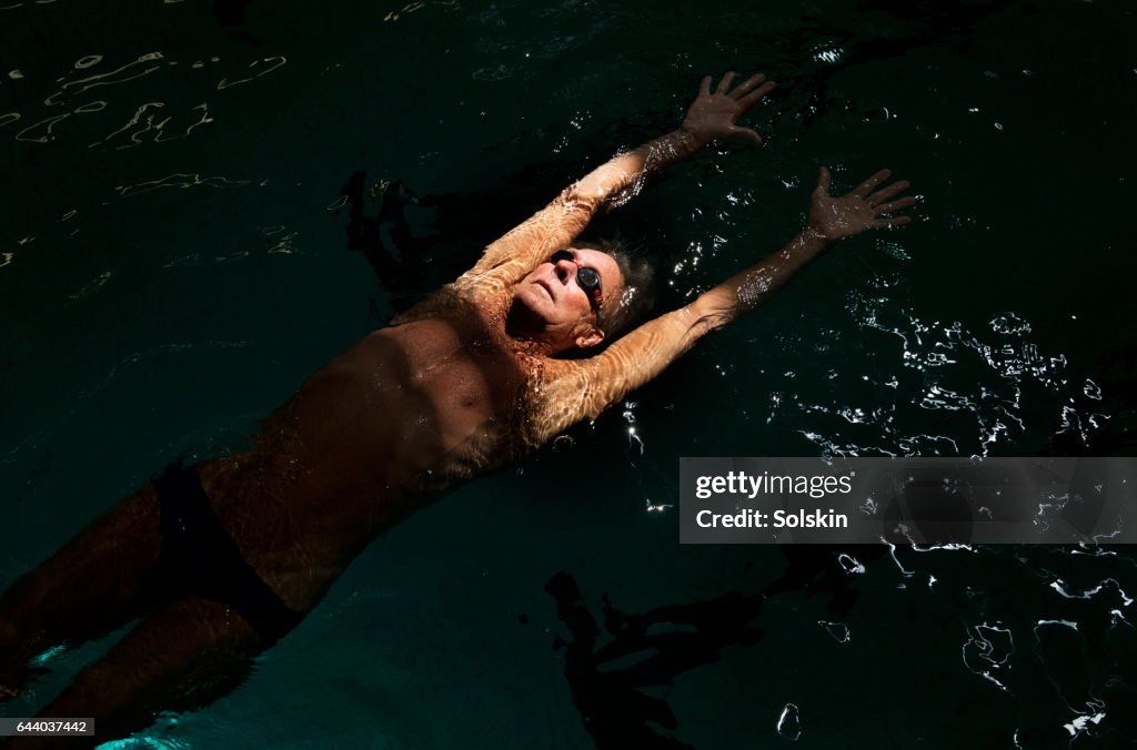 Senior male swimmer stretching out in swimming pool
