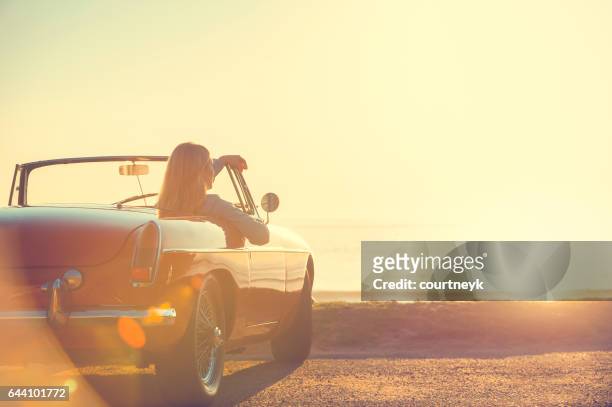 mujer joven en un coche en la playa. - convertible car fotografías e imágenes de stock