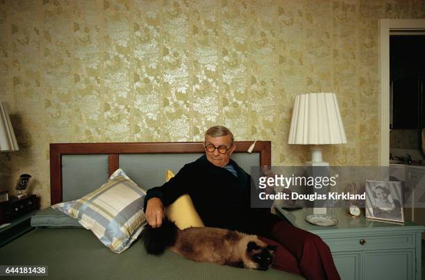 Comedian George Burns smokes a cigar and pets his cat in his bedroom.