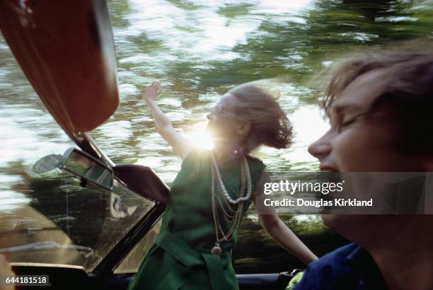 Actress Faye Dunaway hangs out of a convertible as photographer Douglas Kirkland drives with one hand and shoots photos with the other.