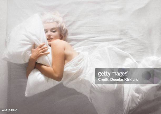 Portrait of American actress Marilyn Monroe as she lies on a bed wrapped in a white sheet, Hollywood, Los Angeles, California, November 1961.