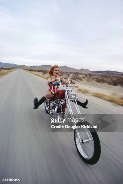 Actress Ann-Margret rides a chopper motorcycle in the desert outside Las Vegas. She wears a shiny star-spangled banner bodysuit. | Location: Near Las...