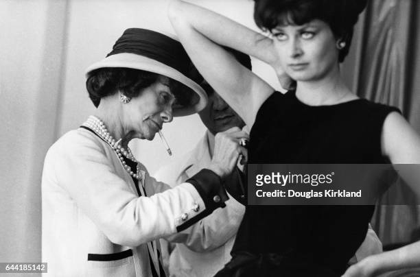 Fashion designer Coco Chanel adjusts the armhole of a model's dress with an assistant.