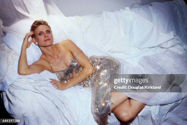 American actress Cindy Pickett wears a silver sequined dress and reclines on a white sofa.