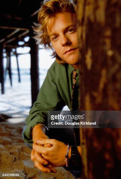 American actor Kiefer Sutherland clasps his hands as he squats under a pier.