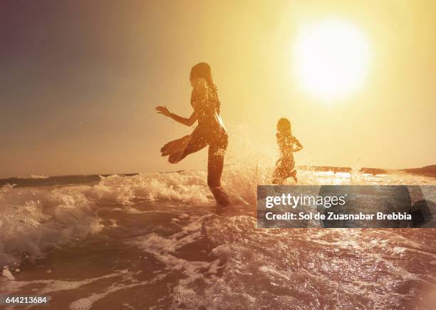 happy girls running to the sea on a beautiful sunset - hot females foto e immagini stock