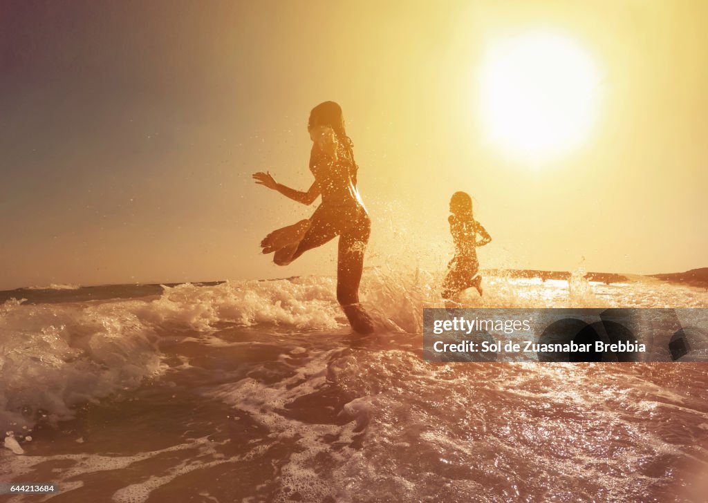 Happy girls running to the sea on a beautiful sunset