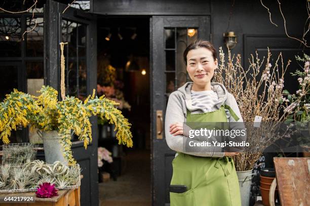 volwassen vrouwelijke bloemist permanent bij de ingang van haar bloemenwinkel. - asia lady selling flower stockfoto's en -beelden