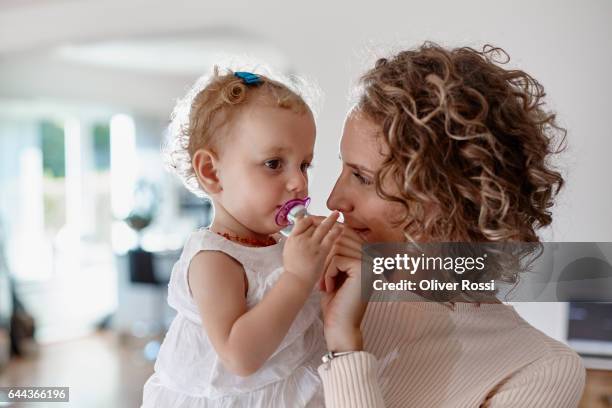 mother holding baby girl with pacifier at home - pacifier stockfoto's en -beelden