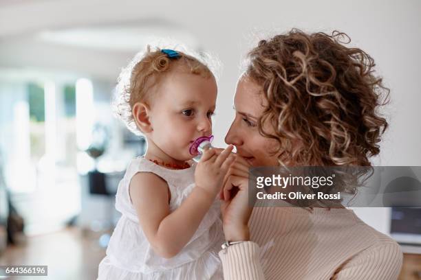 mother holding baby girl with pacifier at home - pacifier stock pictures, royalty-free photos & images