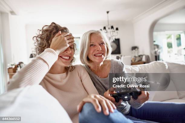 happy mother and adult daughter playing video game at home - mother daughter couch imagens e fotografias de stock
