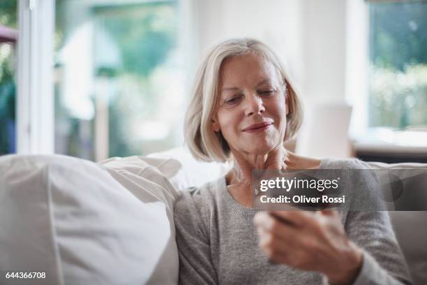 senior woman looking on cell phone at home - sólo mujeres mayores fotografías e imágenes de stock