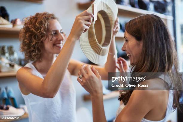 two happy female friends shopping for a hat in a boutique - fashion retail stock pictures, royalty-free photos & images