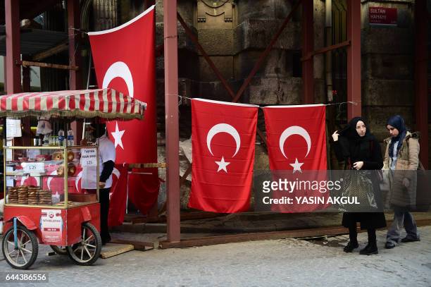 People walk past Turkish national flags as a street vendor sells Turkish traditional backery in the Eminonu district of Istanbul on February 23,...