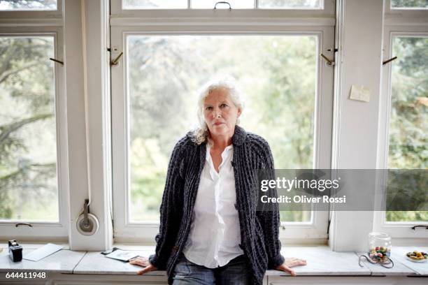 portrait of serious senior woman at the window - waist up stock pictures, royalty-free photos & images