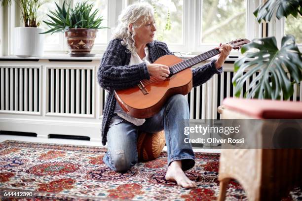 senior woman playing guitar at home - woman playing guitar stock pictures, royalty-free photos & images