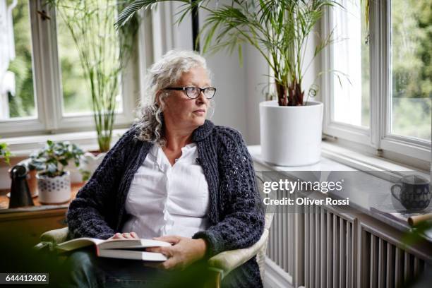 senior woman reading a book at home - senior serious stock pictures, royalty-free photos & images